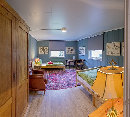 Gemütliches Gästezimmer in Nordland, Norwegen, mit Holzmöbeln, zwei Betten und traditionellen Vogelpostern. Ideal für Angelreisen in Nordland. Warme Beleuchtung und Teppich ergänzen das einladende Ambiente. Perfekter Rückzugsort nach einem Angeltag.