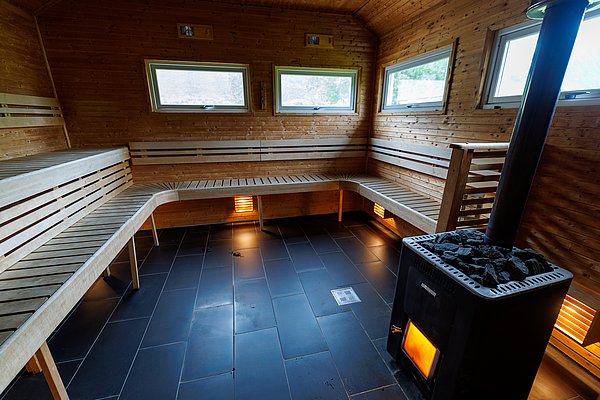 Gemütliche, holzverkleidete Sauna mit drei Fenstern und einem Holzofen in Nord-Norwegen. Perfekt zum Entspannen nach einem erfolgreichen Angelausflug. Ideal für Erholung und Wärme in einer atemberaubenden nordischen Landschaft.