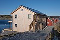 Modernes Holzhaus am Wasser in Hitra, Norwegen. Perfekt für Angelurlaub, mit Panoramablick auf ruhiges Meer. Rote Nebengebäude ergänzen die idyllische Szenerie. Ideal für Erholung und Abenteuer in der skandinavischen Natur.