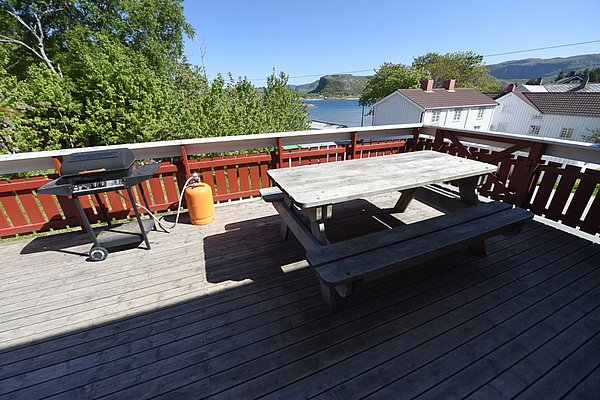 Sonnige Terrasse mit Holztisch und Grill, umgeben von üppigem Grün und malerischem Meerblick in Hitra, Norwegen. Ideal für erholsame Angelpausen. Perfekt für Naturliebhaber und Angler auf der Suche nach Entspannung und Abenteuer.