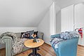 Gemütlicher skandinavischer Wohnraum in Nord-Norwegen mit gestreiftem Sofa, blauer Sessel, Kuscheldecken, Dekokissen mit Widdermotiv. Holzfußboden, helle Holzwände. Kleiner Tisch mit Blumen und Buch. Ideal für Entspannung nach Angelabenteuer.