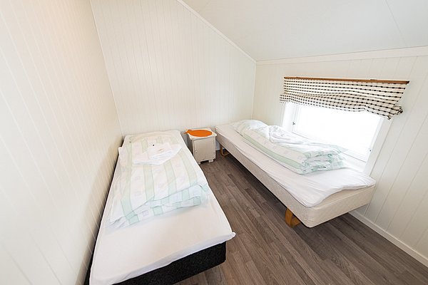 Gemütliches Schlafzimmer in Nordland, Norwegen, mit zwei Einzelbetten, heller Einrichtung und Holzlaminatboden. Perfekt für Angelurlaub; Ruhe und Erholung in skandinavischem Ambiente. Ideal nach spannenden Angeltouren im traumhaften Norwegen.