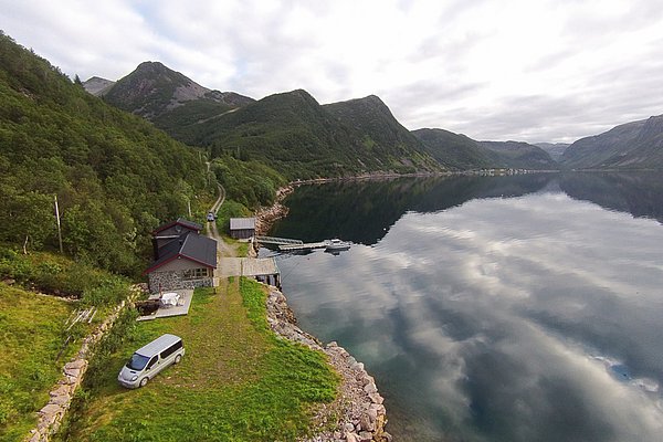 Klares Wasser des norwegischen Fjords in Nord-Norwegen, umgeben von grünen Bergen und einer abgelegenen Hütte. Perfektes Reiseziel für Angelabenteuer und Naturerlebnisse. Ideal für Angelreisen und erholsame Urlaube abseits der Massen.