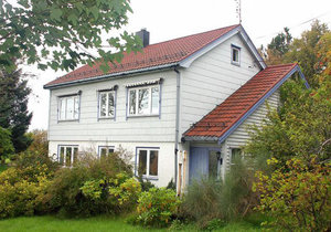 Charmantes, zweistöckiges Haus in Hitra, Norwegen, umgeben von üppigem Grün. Das weiße Holzhaus mit rotem Dach bietet eine gemütliche Basis für Angelurlauber in malerischer Umgebung. Ideal für Naturliebhaber und Abenteurer.