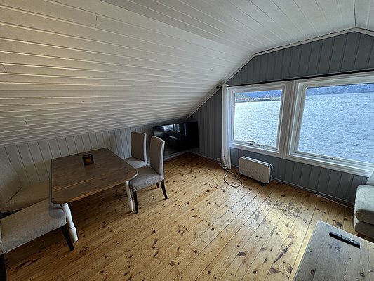 Gemütlicher Raum mit Holzboden, Tisch und Stühlen, großen Fenstern mit Blick auf das klare Wasser von Hitra, Norwegen. Perfekter Rückzugsort für Angler auf Angelreise, um Natur und Entspannung zu genießen.