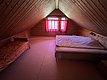 Gemütliches Dachzimmer in Hitra, Norwegen, mit Holzwänden, kleinem Fenster mit roten Vorhängen, Doppel- und Einzelbett. Ideal für ruhige Angelurlaub-Aufenthalte in naturnaher Umgebung. Perfekt zum Entspannen nach erfolgreichen Angeltouren.