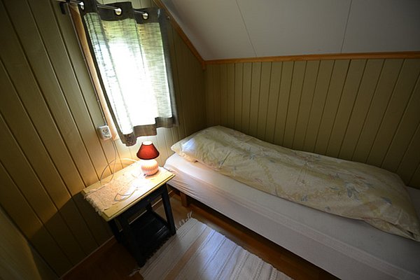 Gemütliches Schlafzimmer in Nordland, Norwegen, mit Einzelbett, Holzvertäfelung und sanftem Lampenlicht. Perfekt für Angelreisende, die nach einem erlebnisreichen Tag Entspannung suchen. Ideale Unterkunft für Angelurlaub in Skandinavien.