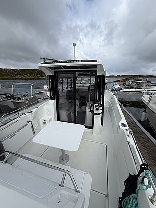 Moderne Angelboot-Auswahl in Süd-Norwegen: Ein "Merry Fisher"-Boot wartet am Steg mit einladendem Deck, ideal für Meeresangeln. Wolkiger Himmel und felsige Küsten im Hintergrund. Perfekter Ausgangspunkt für Angelabenteuer.
