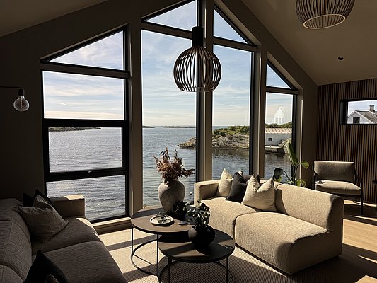 Gemütliches Wohnzimmer in Südwest-Norwegen mit Panoramafenstern, die den Blick auf das malerische Meer und die Küste freigeben. Moderne Einrichtung sorgt für entspannte Urlaubsatmosphäre. Perfekt für eine Angelreise in atemberaubender Natur.