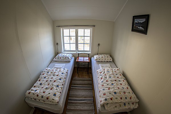 Gemütliches Schlafzimmer in Nord-Norwegen mit zwei Einzelbetten, hellem Fenster und traditionellem Dekor. Ideal für Angler, die nach einem Tag voller Abenteuer Erholung suchen. Perfekt für Angelreisen in unberührter Natur.