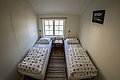 Gemütliches Schlafzimmer in Nord-Norwegen mit zwei Einzelbetten, hellem Fenster und traditionellem Dekor. Ideal für Angler, die nach einem Tag voller Abenteuer Erholung suchen. Perfekt für Angelreisen in unberührter Natur.