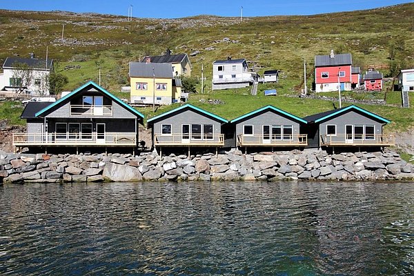 Gemütliche Ferienhäuser am Wasser in Nord-Norwegen, eingebettet in eine grüne Hügellandschaft. Perfekter Ausgangspunkt für Angelreisen und Naturerkundungen. Friedliche Kulisse mit klarer Luft und beeindruckender Umgebung. Ideal für Erholung und Abenteuer.