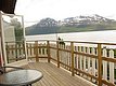 Holzterrasse mit Tisch und Stühlen, Blick auf norwegische Fjordlandschaft und schneebedeckte Berge. Perfekter Ort für Entspannung und Naturgenuss in Nord-Norwegen. Ideal für Angelreisen und Erholung.