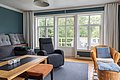 Gemütliches Wohnzimmer in Hitra, Norwegen, mit großen Fenstern, die auf eine grüne Landschaft blicken. Moderne, bequeme Möbel und ein Holztisch schaffen eine entspannte Atmosphäre. Ideal für Erholung nach einem erfolgreichen Angelausflug.