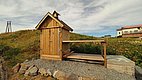 Kleines, hölzernes Gebäude auf Kiesboden in der idyllischen Landschaft Nordlands, Norwegen. Der blaue Himmel ergänzt die ruhige, naturnahe Umgebung. Perfekt für Angelreisende, die unberührte Natur und Ruhe suchen.