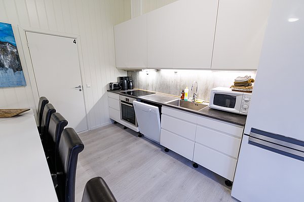 Moderne Küche in Nordland, Norwegen: Weiße Schränke, schwarze Arbeitsplatten, Geschirrspüler, Mikrowelle und Kaffeemaschine. Helles Holzlaminat schmiegt sich an stilvolle Barhocker. Ideal für Angelreisen zur Selbstverpflegung. Perfekt für gemütliche Abende nach erfolgreichen Angeltagen.