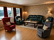 Gemütliches Wohnzimmer in Hitra, Norwegen: Ledersofas, Sessel, Couchtisch und Vintage-Tapete. Fenster bieten Blick auf beeindruckende Berg- und Seenlandschaft. Perfekte Unterkunft für erholsamen Angelurlaub in der Natur. Ideal zum Entspannen nach einem erfolgreichen Angeltag.