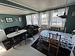 Gemütliches Wohnzimmer in Hitra, Norwegen, mit Holzwänden, Sofaecke, Esstisch mit geblümter Tischdecke und großen Fenstern mit Blick aufs Meer. Perfekt für einen entspannten Angelurlaub in malerischer Umgebung.