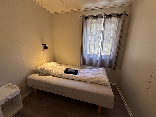 Gemütliches, schlicht eingerichtetes Schlafzimmer in Hitra, Norwegen. Einzelbett mit Leselampe, Fenster mit Vorhang. Ideal für Angelurlaub, Ruhe und Entspannung in der Natur. Entdecke die fischreichen Gewässer der Umgebung.