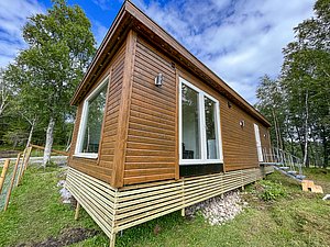 Holzhaus in Nordland, Norwegen: modernes Ferienhaus in waldreicher Umgebung. Ideal für Angelurlaub und Outdoor-Abenteuer. Große Fenster mit Blick ins Grüne, perfekter Rückzugsort für Naturfreunde. Ruhige Lage für Entspannung und Erholung.