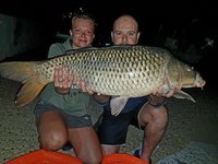 Zwei Personen präsentieren bei Nacht stolz einen großen Karpfen.