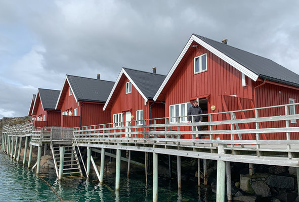 Rote Holzhäuser auf Stelzen in Nordland, Norwegen, am Wasser. Perfekter Ausgangspunkt für Angelabenteuer im Norden, umgeben von malerischer Landschaft. Ideal für Angelreisen und Naturliebhaber.