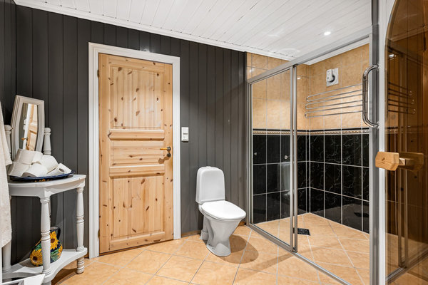 Badezimmer in Südwest-Norwegen: Elegantes Interieur mit Holz- und Fliesenelementen, Glastüren für Dusche und Sauna. Helle, moderne Gestaltung, ideal für Erholung nach einem erlebnisreichen Tag beim Angeln. Perfekte Kombination aus Komfort und skandinavischem Stil.