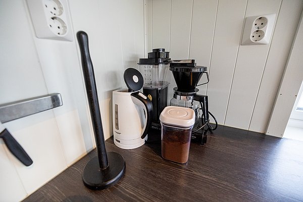Küchenecke mit Wasserkocher, Kaffeemaschine und Behälter auf dunklem Holz. Perfekte Ausstattung für Angelurlaub in Hitra, Norwegen. Gemütliches Frühstück nach erfolgreichem Angeltag. Ideal für Erholung und Komfort im skandinavischen Stil.