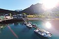 Nord-Norwegen: Malerisches Fjorddorf mit traditionellen Holzhäusern am Wasser. Boote an einem Steg, von Bergen umgeben, im Sonnenlicht glitzernd. Ideal für Angelreisen und Naturerlebnis.