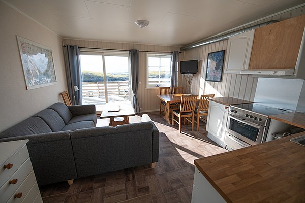 Gemütliches Ferienhaus in Nordland, Norwegen: heller Wohnbereich mit Küche, Esstisch, Sofa, TV und großer Fensterfront mit Blick auf die Natur. Ideal für einen entspannten Angelurlaub.