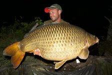 Ein Angler hält einen großen Karpfen in den Händen, während er in der Nacht im Freien posiert.