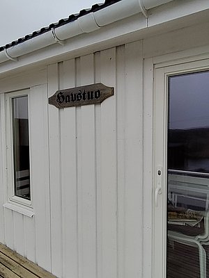 Holzhäuser in Nordland, Norwegen, mit traditionellem skandinavischen Design. Weiße Fassade und Schild mit "Havstuo" weisen auf gemütliche Unterkünfte hin, ideal für Angelreisen und Erholung. Geräusche des Meeres sorgen für entspannte Atmosphäre.