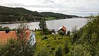 Malerische Landschaft in Hitra, Norwegen: Blick auf ruhigen Fjord, bewaldete Hügel, traditionelle weiße und rote Häuser, ideal für Angelurlaub und Naturerlebnisse. Perfekter Ort für Outdoor-Aktivitäten und Entspannung am Wasser.