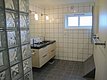 Modernes Badezimmer in Nord-Norwegen mit weißen Fliesen, Glasbausteinwand, Waschbecken und kleinem Fenster, bietet Komfort und skandinavisches Design für Angelreisende. Ideal für Erholung nach einem erfolgreichen Tag am Wasser.