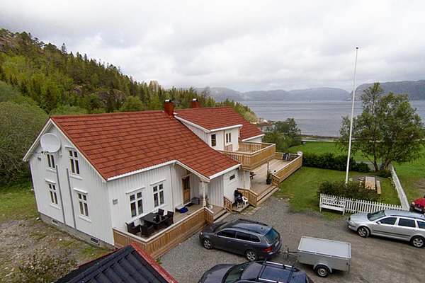 Ein gemütliches, traditionelles, weißes Haus mit roten Ziegeldach, umgeben von grüner Natur und malerischem Blick auf das Meer in Hitra, Norwegen. Perfekt für einen entspannten Angelurlaub in skandinavischer Idylle.