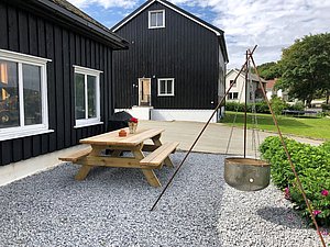Gemütlicher Hof in Hitra, Norwegen: Holzbank und Feuerschale auf Kiesfläche, ideal für erholsame Angelreisen. Umgeben von traditionell-skandinavischen Häusern, grünem Rasen und blühenden Büschen – perfekte Kombination aus Natur und Komfort.