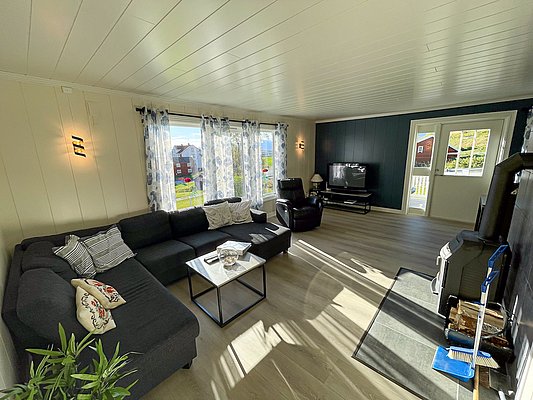 Helles, gemütliches Wohnzimmer in Nord-Norwegen mit großer Eckcouch, Sessel, Fernseher, Kamin und Tageslicht. Ideal für Entspannung nach einem Angeltag in atemberaubender Naturkulisse. Perfekte Unterkunft für Angelurlaub in Skandinavien.