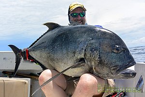 Ein Angler hält einen gigantischen Fisch auf einem Boot vor der Küste Panamas. Der strahlende Himmel im Hintergrund verstärkt das beeindruckende Erlebnis des Meeresangelns an der Tuna Coast.