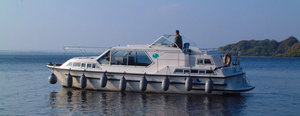 Hausboot gleitet auf dem River Shannon, Irland. Ideal für Angelurlaub und Erkundungen. Ruhiges Wasser, umgeben von sanften Hügeln, bietet perfekten Rückzugsort für Angler. Entdecke die Schönheit und Vielseitigkeit irischer Wasserwege.