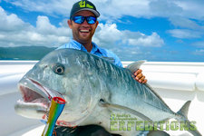 Ein Angler hält einen großen Giant Trevally auf einem Boot in Tansania. Klarer Himmel und Meer im Hintergrund. Perfekte Bedingungen für einen unvergesslichen Angelurlaub voller Abenteuer und großartiger Fänge.