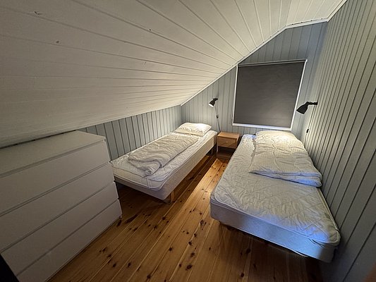 Gemütliches Schlafzimmer mit zwei Einzelbetten in einem charmanten, holzverkleideten Ferienhaus in Hitra, Norwegen. Ideal für Angelurlaub in der Region; bietet Komfort und Erholung nach einem erfolgreichen Angeltag.