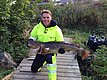 Ein Angler hält stolz einen großen Fisch in Hitra, Norwegen. Umgeben von üppiger Natur, symbolisiert das Bild die erfolgreiche Angelreise und eindrucksvolle Fänge dieser Region. Ideal für Meeresangeln-Abenteuer.