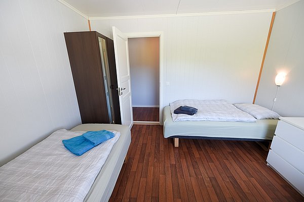 Gemütliches Schlafzimmer in Hitra, Norwegen, mit zwei Betten, Holzfußboden und heller Wandgestaltung. Ideal für erholsamen Angelurlaub in ruhiger Umgebung. Perfekter Rückzugsort nach spannenden Angeltagen.
