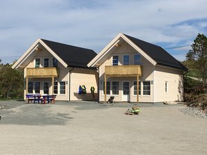 Zwei moderne Holzhäuser mit schwarzen Dächern in Hitra, Norwegen, sonnenbeschienen. Perfekt für Angelurlaube, bietet sie Entspannung und fantastische Fangchancen. Umgebung: Natur pur und Abenteuer in malerischer Landschaft.