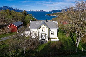 Ländliches Haus in Nordland, Norwegen, umgeben von grüner Landschaft und Fjorden, Bergkulisse im Hintergrund. Ideal für Erholung und Angelreisen in malerischer Natur. Petri Heil – sorglos angeln weltweit.