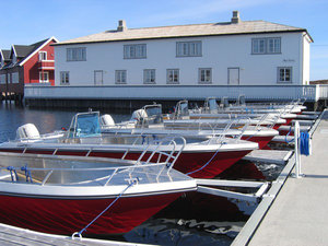 Boote im Hafen von Hitra, Norwegen, vor einem weißen Gebäude. Ideal für Angelurlaub und Meeresangeln. Ruhige Umgebung lädt zum Entspannen und Entdecken ein. Perfekter Ausgangspunkt für Abenteuer auf dem Wasser mit hoher Fangchance.