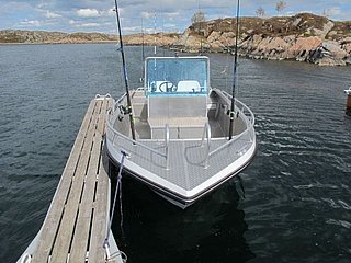 Ein modernes Angelboot liegt an einem Steg in einem ruhigen Gewässer mit felsiger Küste im Hintergrund – ideal für einen Angelurlaub in Tansania.