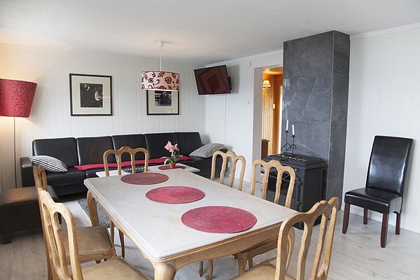 Gemütliches Wohnzimmer in Nord-Norwegen: Helle Holzmöbel, Kamin, dekorative rote Akzente. Ideal zum Entspannen nach Angelabenteuern. Perfekte Kombination aus skandinavischem Design und Funktionalität. Perfekter Ausgangspunkt für unvergessliche Angelreisen in Nord-Norwegens spektakulärer Natur.