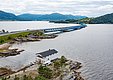 Küstenlandschaft von Hitra, Norwegen: Ein modernes Brückensystem überspannt das ruhige Wasser, umgeben von grünen Hügeln. Ein charmantes Haus steht nahe der Küste und verspricht Abenteuer und Erholung. Perfekt für Angelreisen.