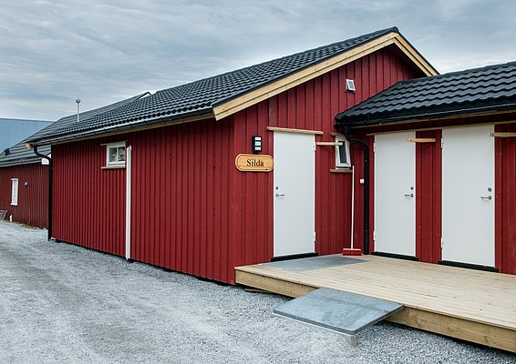 Ein rotes Gebäude mit schwarzen Dächern und einer Holzrampe, beschriftet mit "Silda".